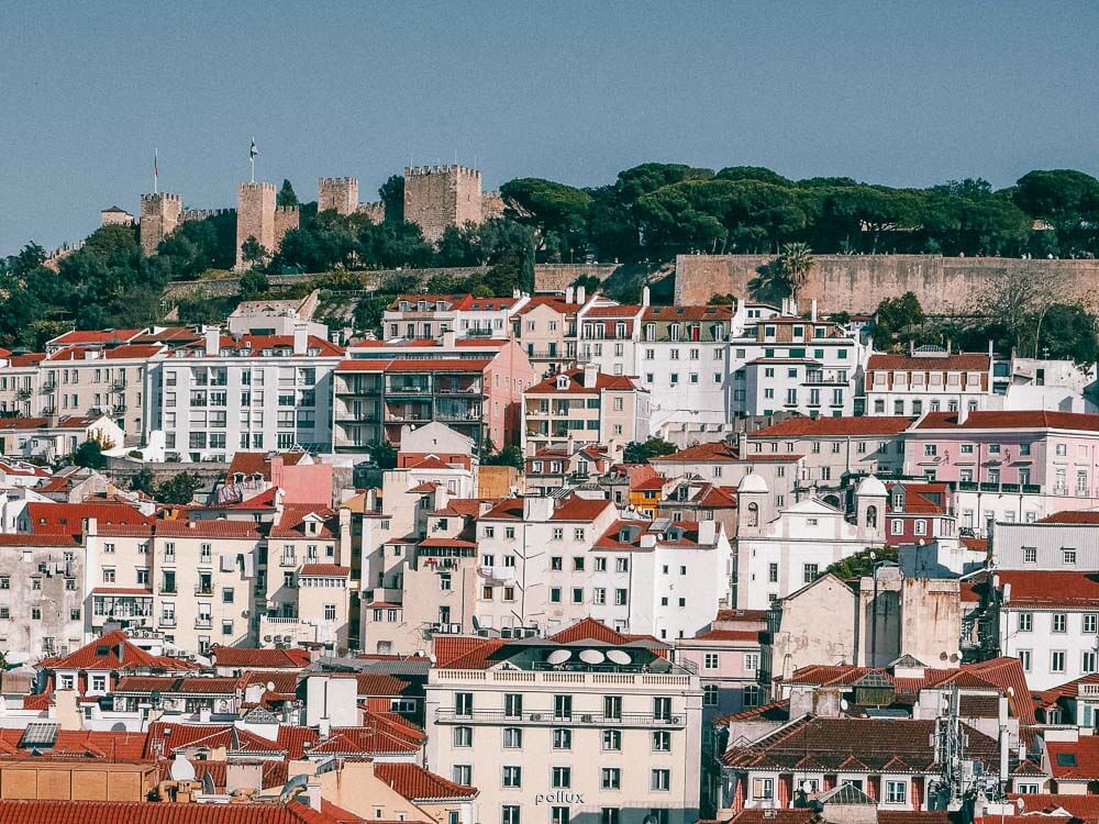 View of the Alfama neighborhood, with white buildings with red roofs and St. George’s Castle above everything. 