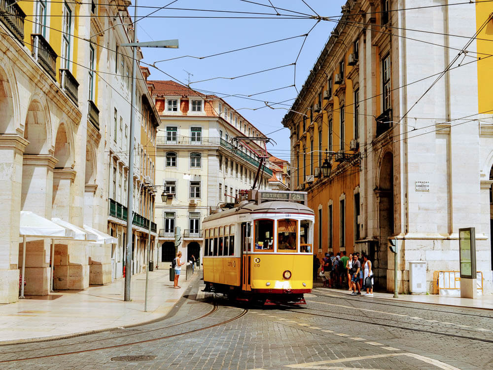 A yellow and white tram in a street in Lisbon, surrounded by buildings during the daytime.