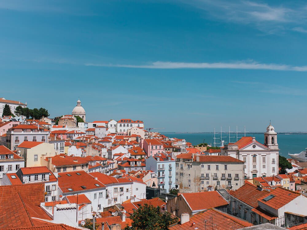 Aerial view of Lisbon, Portugal with colorful buildings with red roofs and the Tagus River in the background.