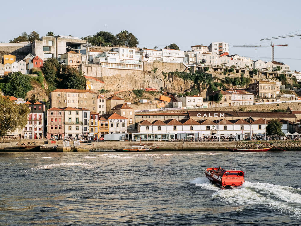 A river scene featuring a boat and Porto in the backdrop.