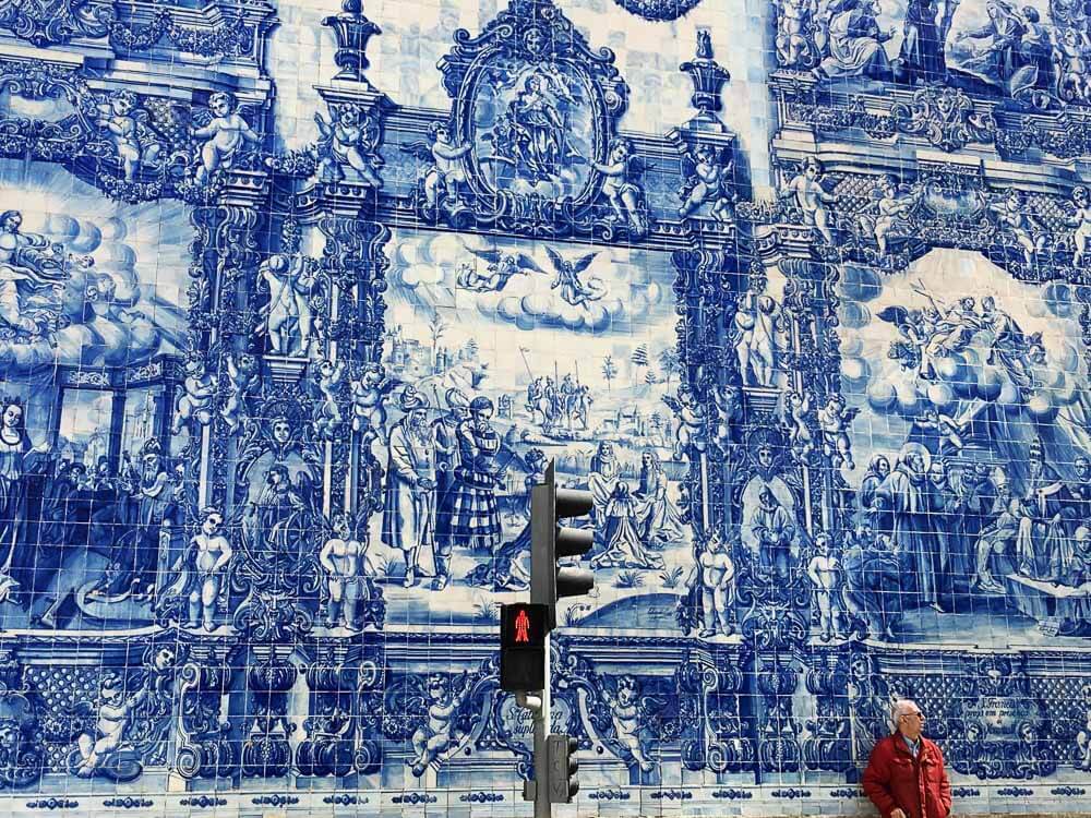 A man in a red jacket standing in front of a blue and white tile wall in Porto.