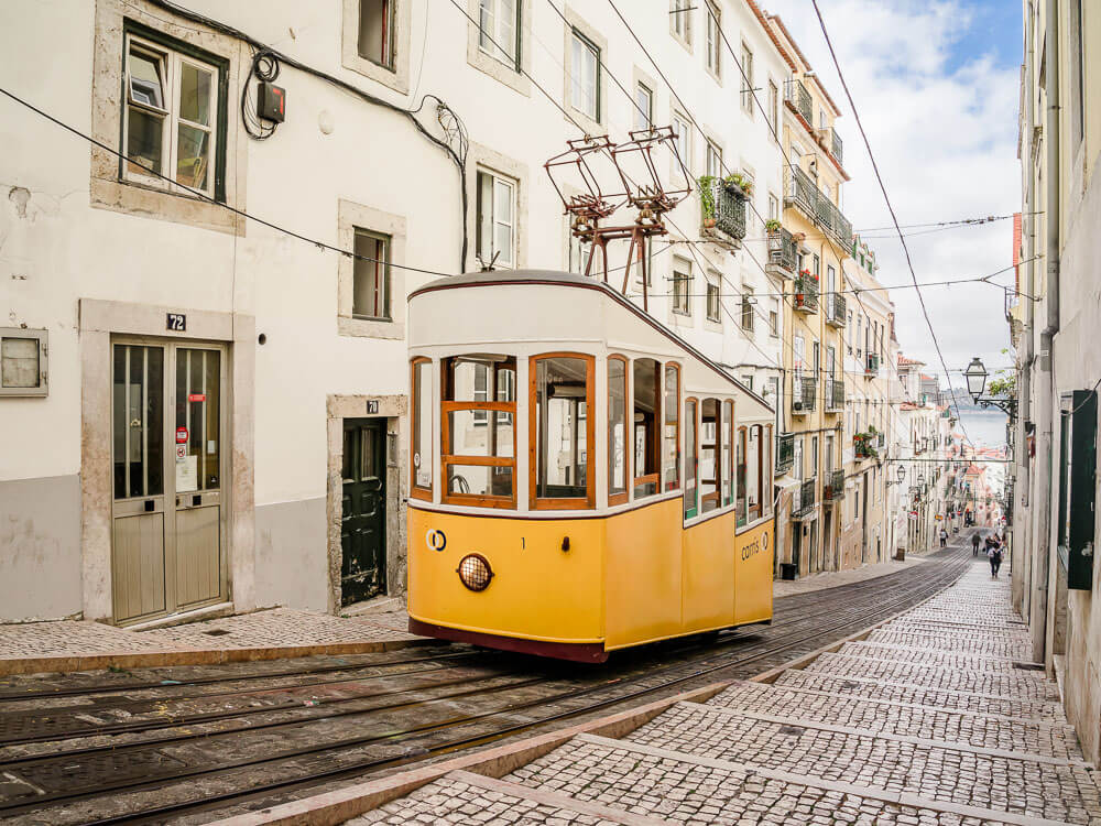 A yellow and white tram on a narrow street, surrounded by buildings.