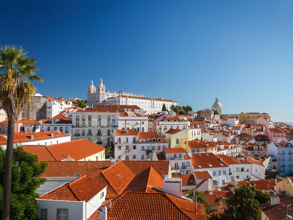 Aerial view of Lisbon's cityscape with colorful buildings with red roofs and a clear sky.