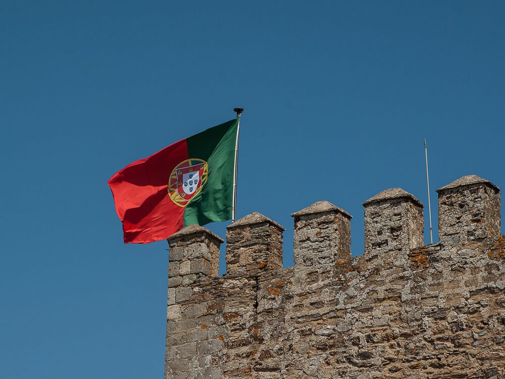 A Portuguese flag waving high on a city tower.