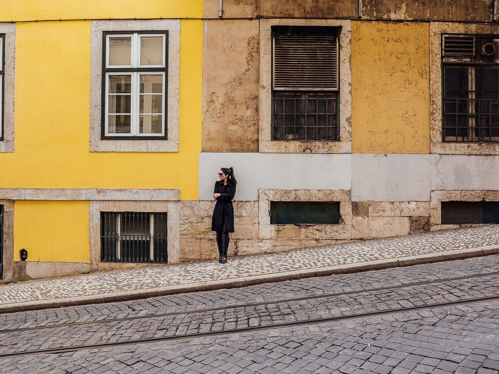 A woman standing on a street in front of a yellow building.