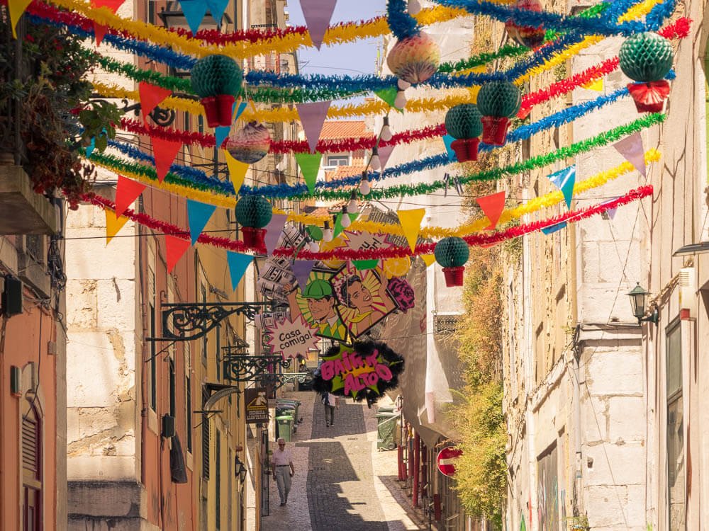 A narrow ancient street in Portugal adorned with colorful hanging decorations.