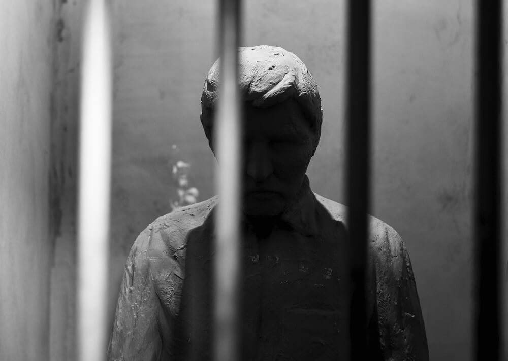 Black-and-white image of a statue of a person behind bars, in the cell of the Aljube Museum.