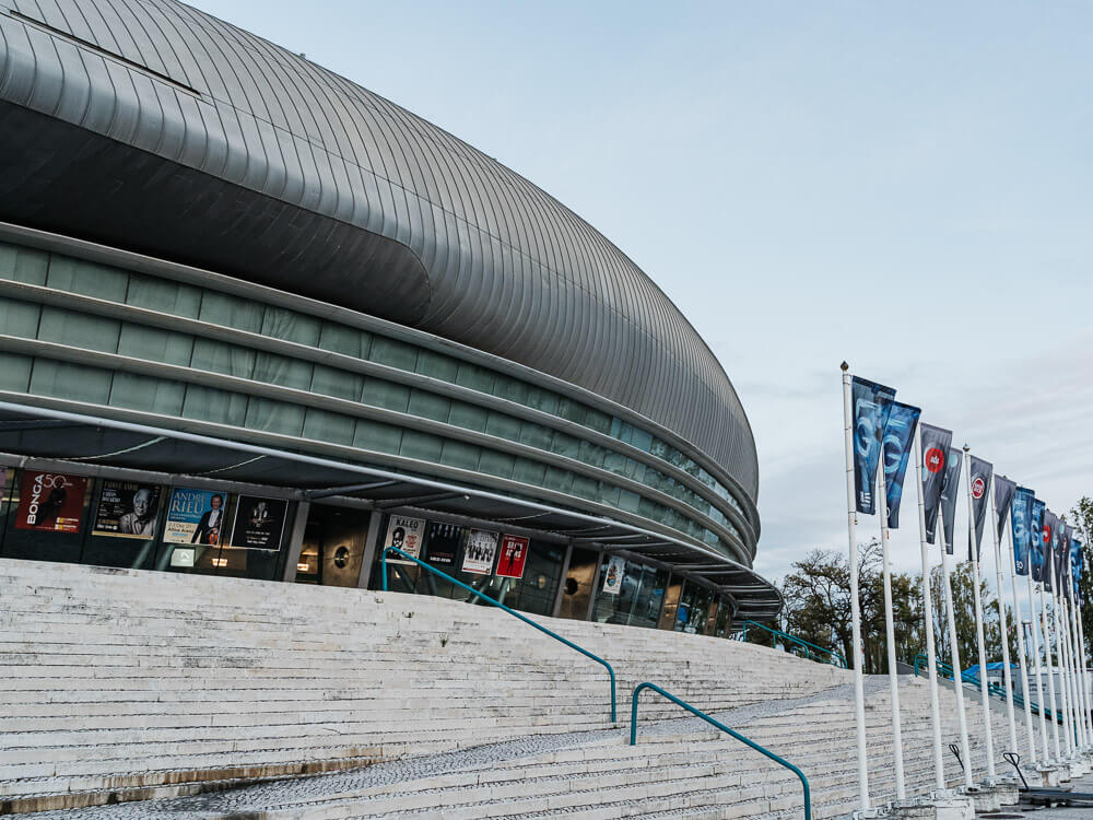 Exterior of the Altice Arena, with a concrete staircase and various little flags on the right. There are posters showing upcoming events.