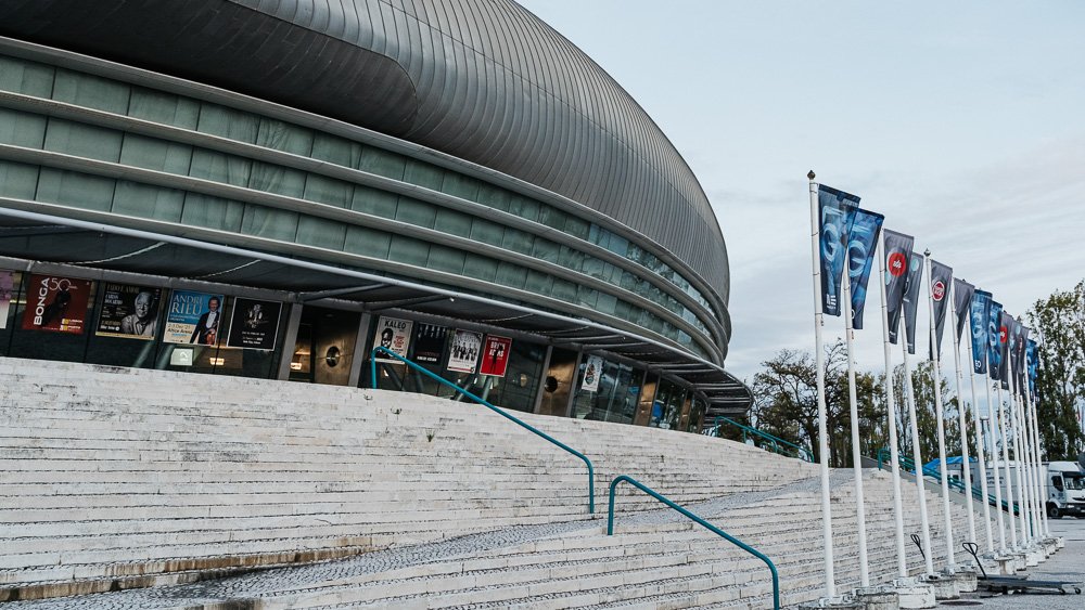 Exterior of the Altice Arena, with a concrete staircase and various little flags on the right. There are posters showing upcoming events.