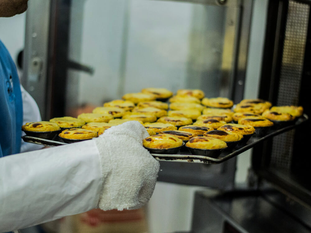 A man with gloves holding a tray of pastéis de nata.