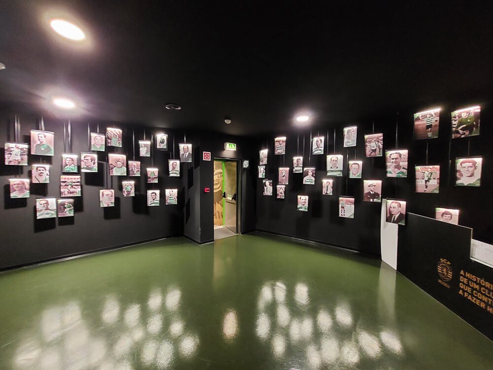 A black room with green flooring, with several photos of athletes hanging on the walls. In the background, there is a glass door.