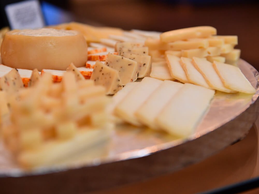 A board with various different cheeses sliced.