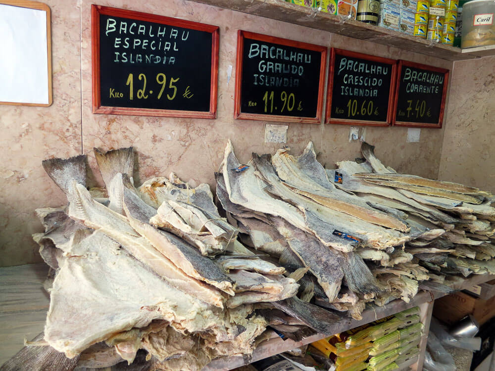 A shop selling salted codfish. There are several stacks of fish, and above, on the wall, signs indicating the prices.