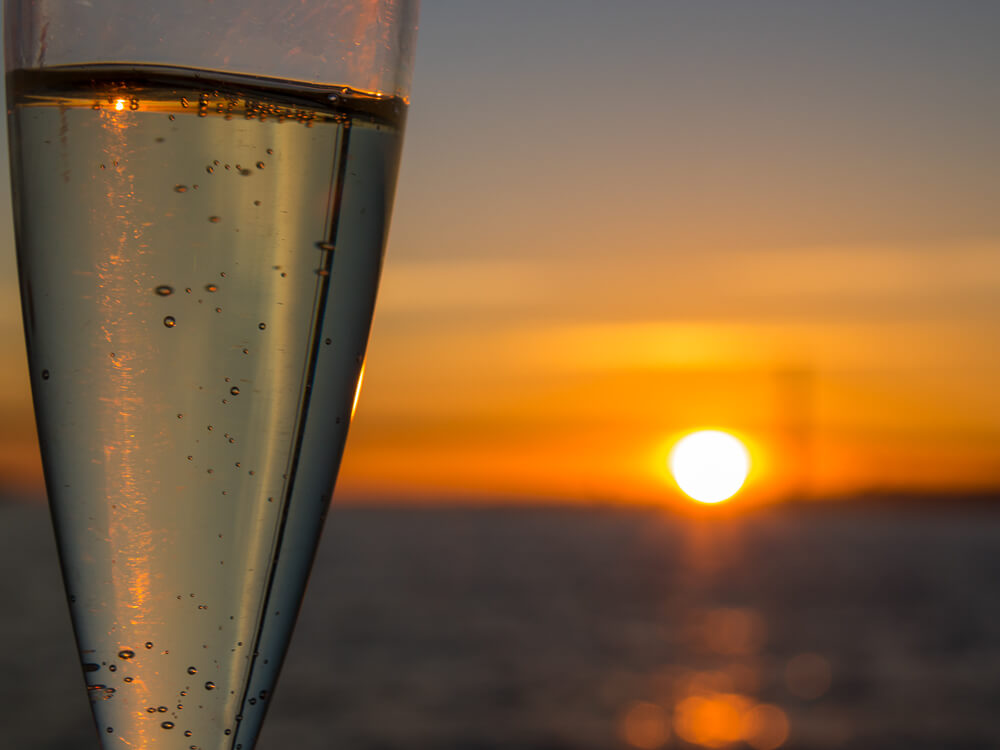 A glass of sparkling wine with the Tagus River and the sunset blurred in the background.