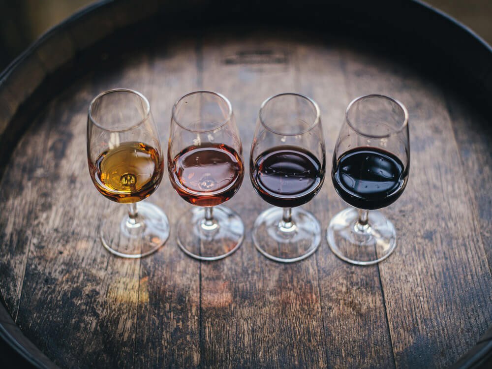 Four glasses with different types of port wine arranged in a horizontal line on top of a wooden barrel.