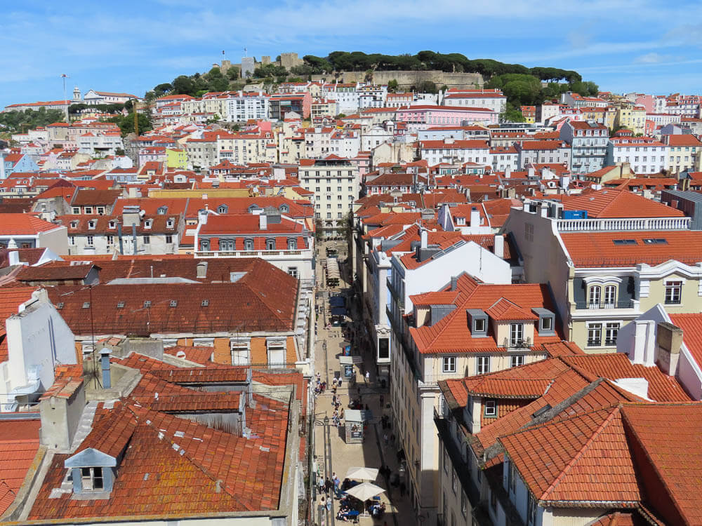 A panoramic view of Lisbon's red-tiled rooftops, with the historic São Jorge Castle perched on a hill in the background.