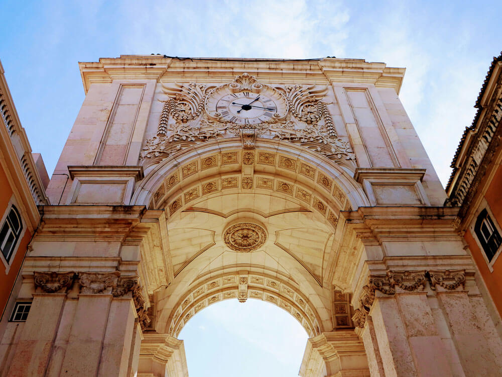 The majestic Arco da Rua Augusta, a grand archway in Lisbon's downtown area, viewed from below against a clear blue sky.