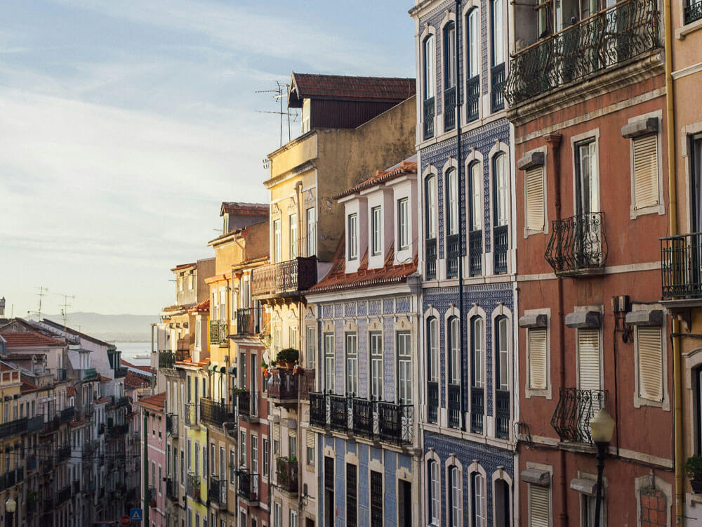 A picturesque row of colorful, traditional buildings in Lisbon, with intricate balconies and sunlight casting warm hues on the facades.