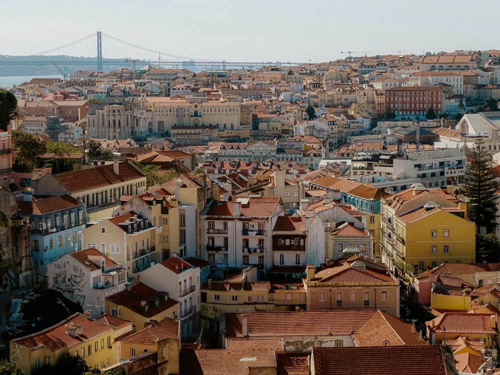 An expansive view of Lisbon's historic neighborhoods and the 25 de Abril Bridge, highlighting the city's unique architecture and layout.