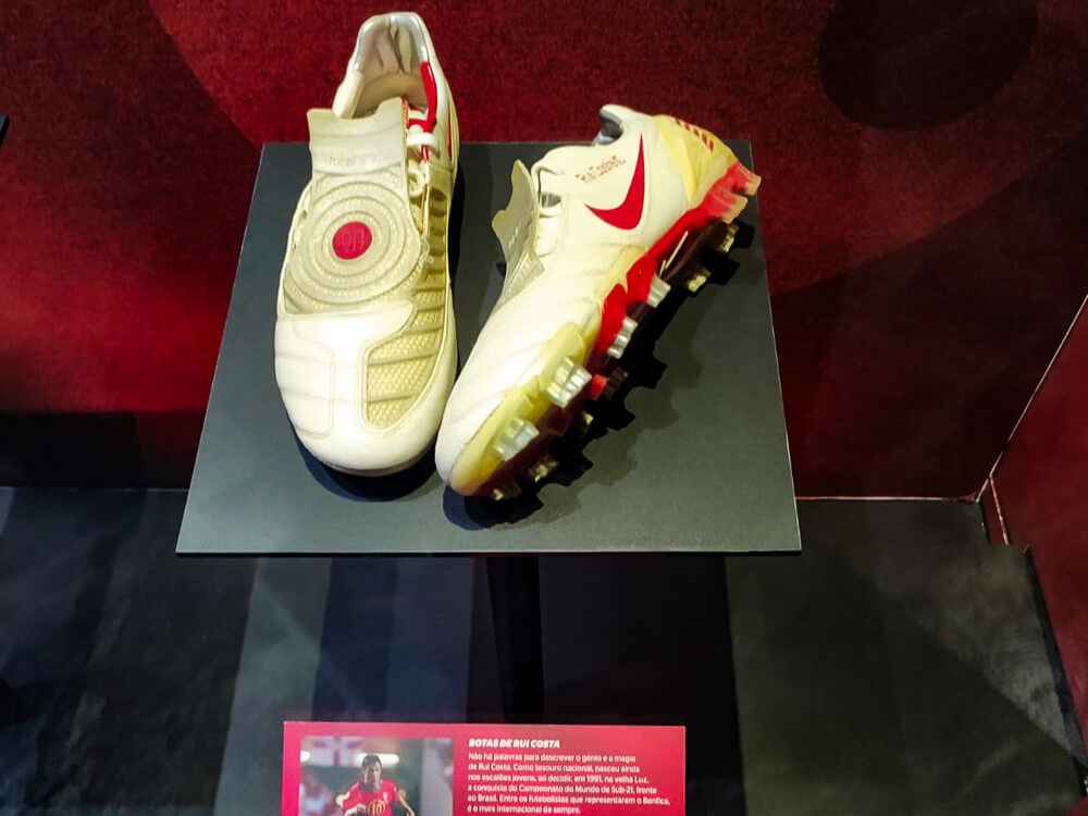 A display of Rui Costa's soccer shoes at a museum, showcasing the iconic player's gear with a red Nike swoosh and personalized details.