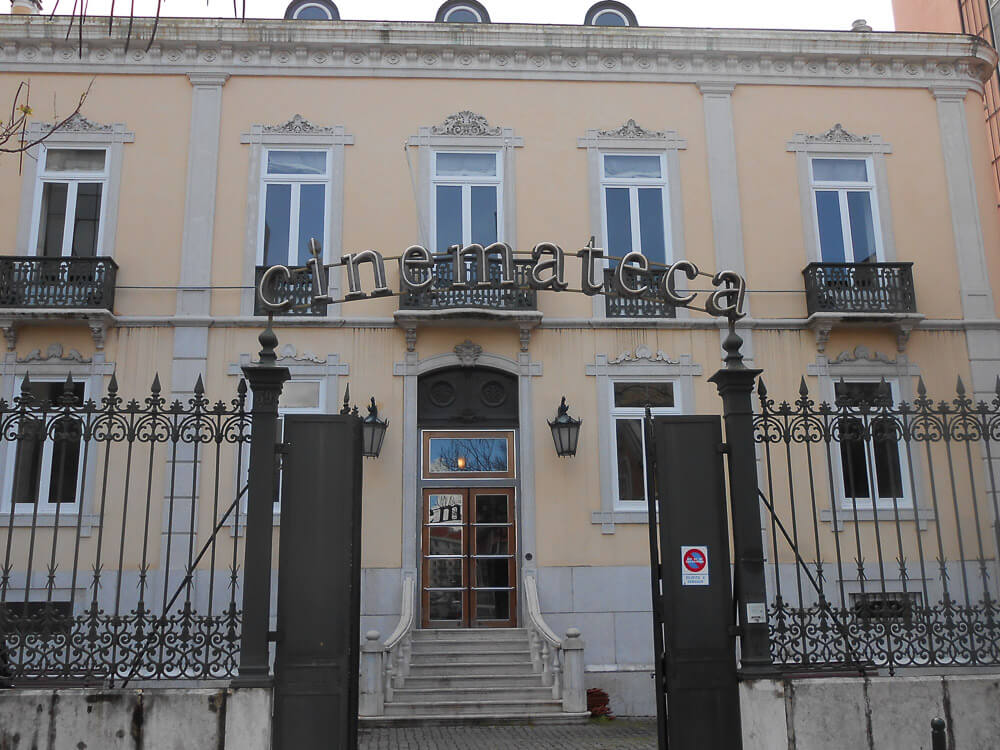 The front of a building labeled "Cinemateca," featuring an elegant façade with iron balconies and gated entrance.