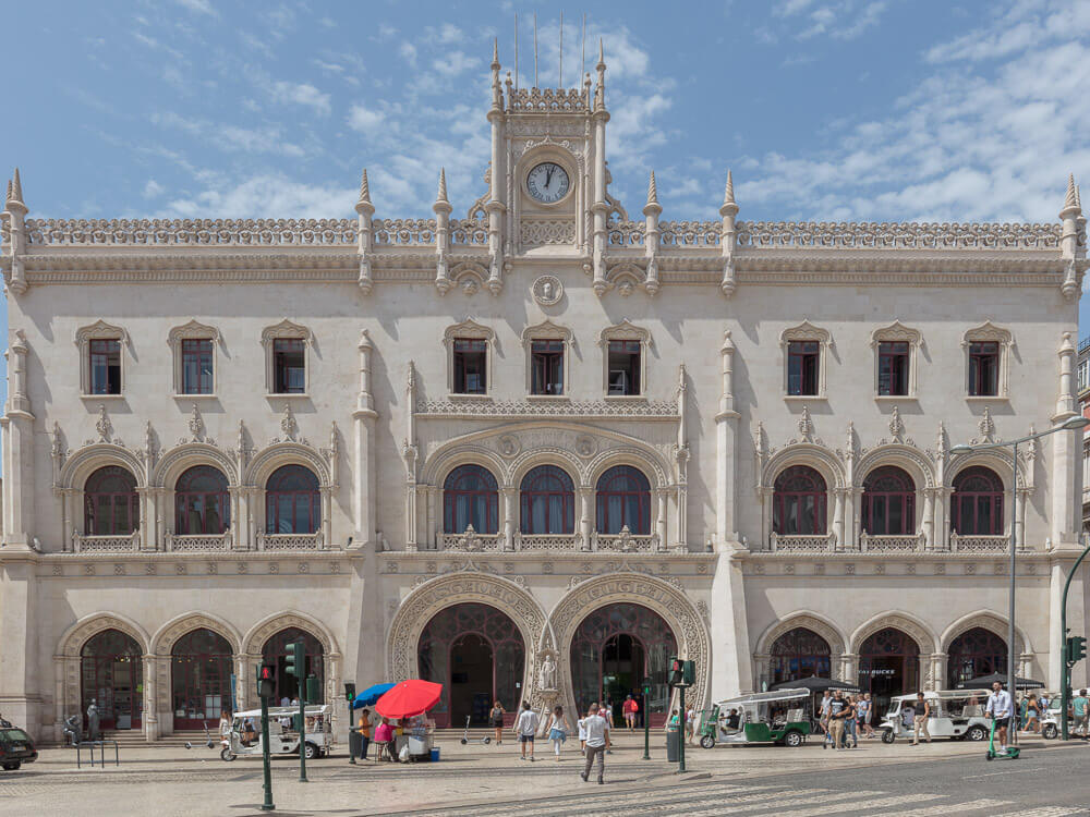 The ornate facade of Rossio Railway Station in Lisbon, featuring intricate stonework and arches, a fine example of neo-Manueline architecture.