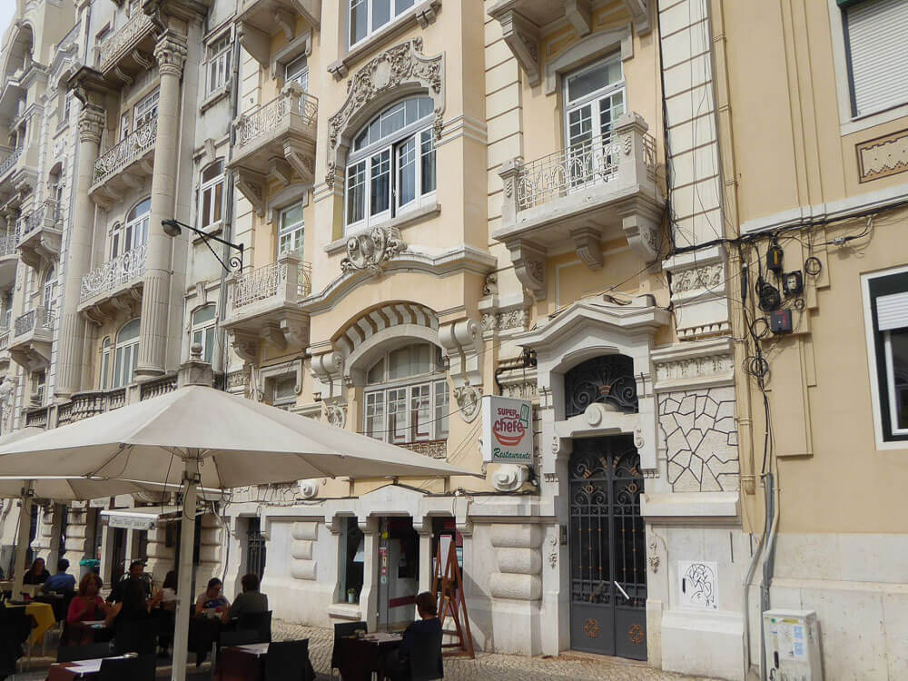 Close-up of a building façade with intricate architectural details, outdoor café seating in the foreground.