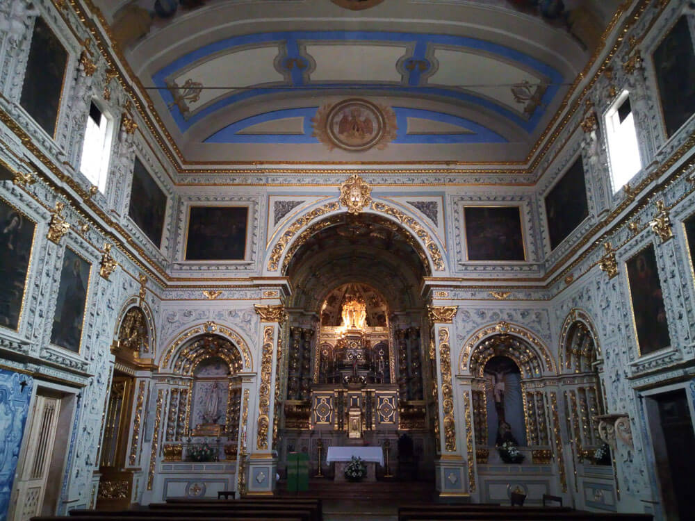 Ornate church interior with elaborate gold details, arches, and a richly decorated altar.