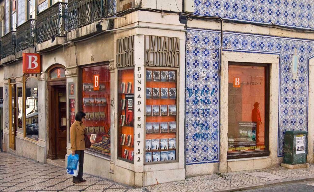 The exterior of Livraria Bertrand, the oldest operating bookstore in the world, located in Lisbon. The building features traditional Portuguese azulejos and a display of books in the windows.