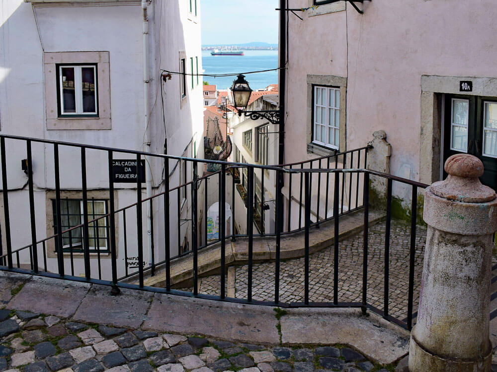 A narrow alleyway in Lisbon with traditional houses and a metal railing along the cobblestone steps.