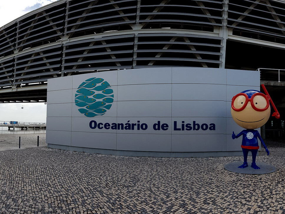 The exterior of the Lisbon Oceanarium, with its distinctive architecture and the official mascot welcoming visitors.