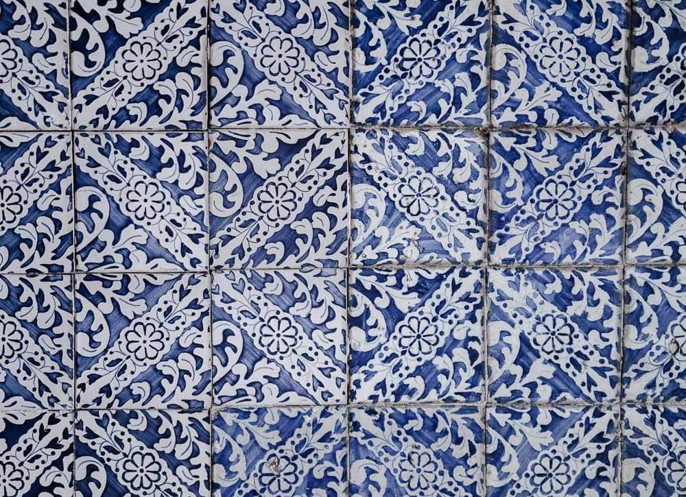 A close-up view of traditional Portuguese azulejo tiles, featuring a repetitive pattern of intricate blue and white floral and geometric designs.