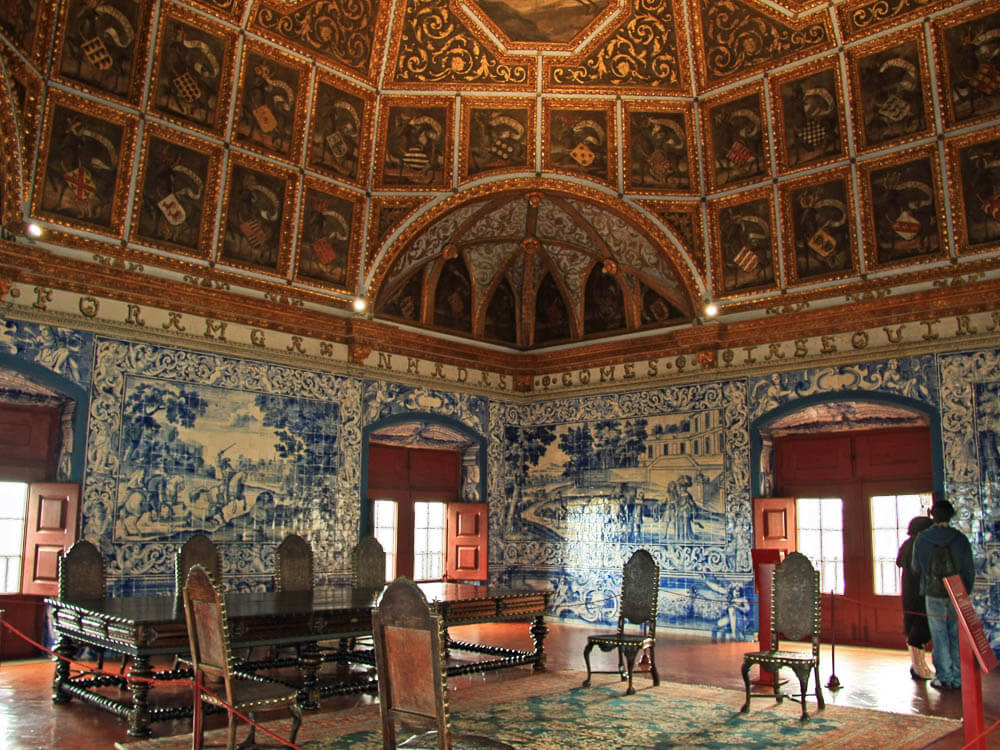 A richly decorated room inside the National Palace of Sintra, showcasing elaborate azulejo tile murals and a beautifully painted wooden ceiling.