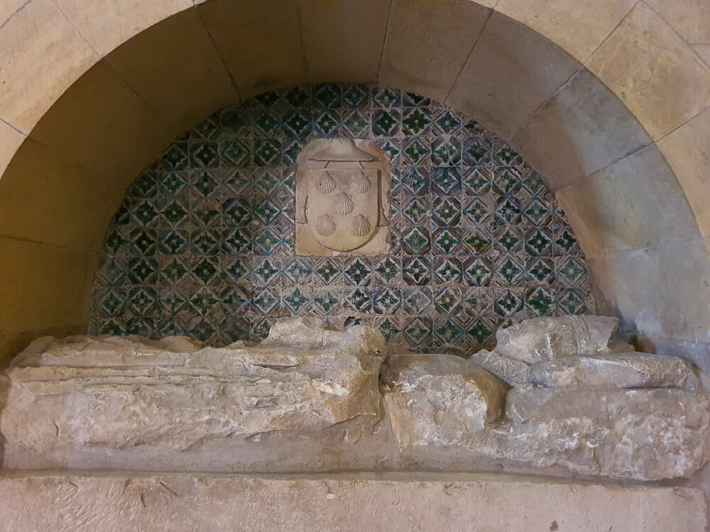 A historical alcove with patterned azulejo tiles in green and blue, featuring a stone sculpture with a coat of arms, within a Lisbon building.