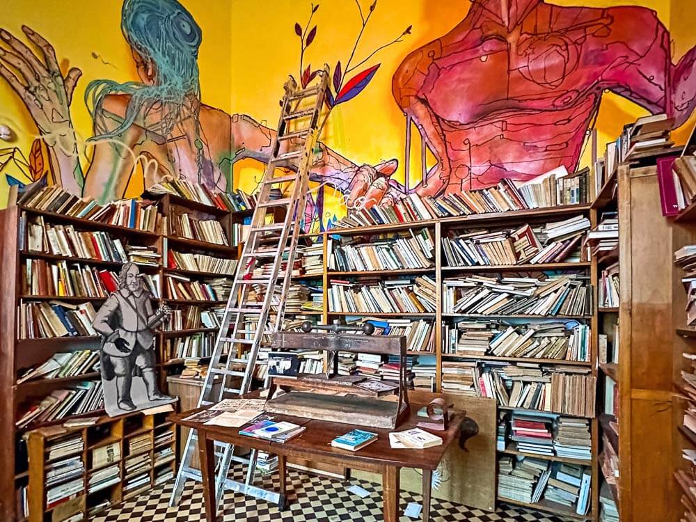 Interior of a bookstore in Marvila, Lisbon, with walls covered in colorful murals and shelves filled with books, alongside a ladder for reaching higher shelves.