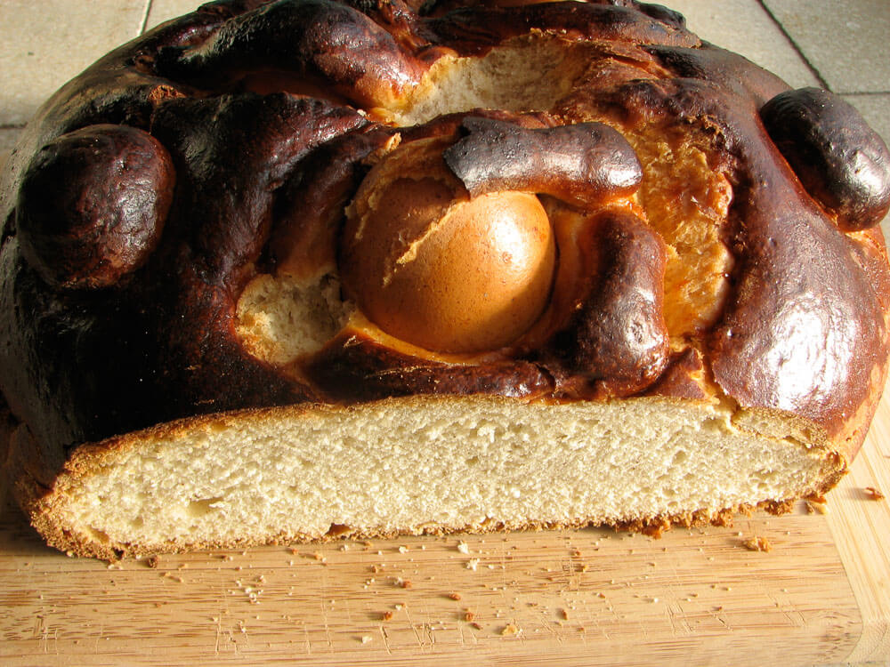 An Easter Bread, with a boiled egg on top, cut in half on a wooden board.

