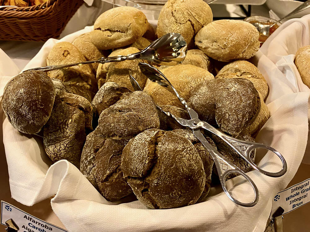 A basket with a white cloth and two tongs. Inside, there are carob breads.