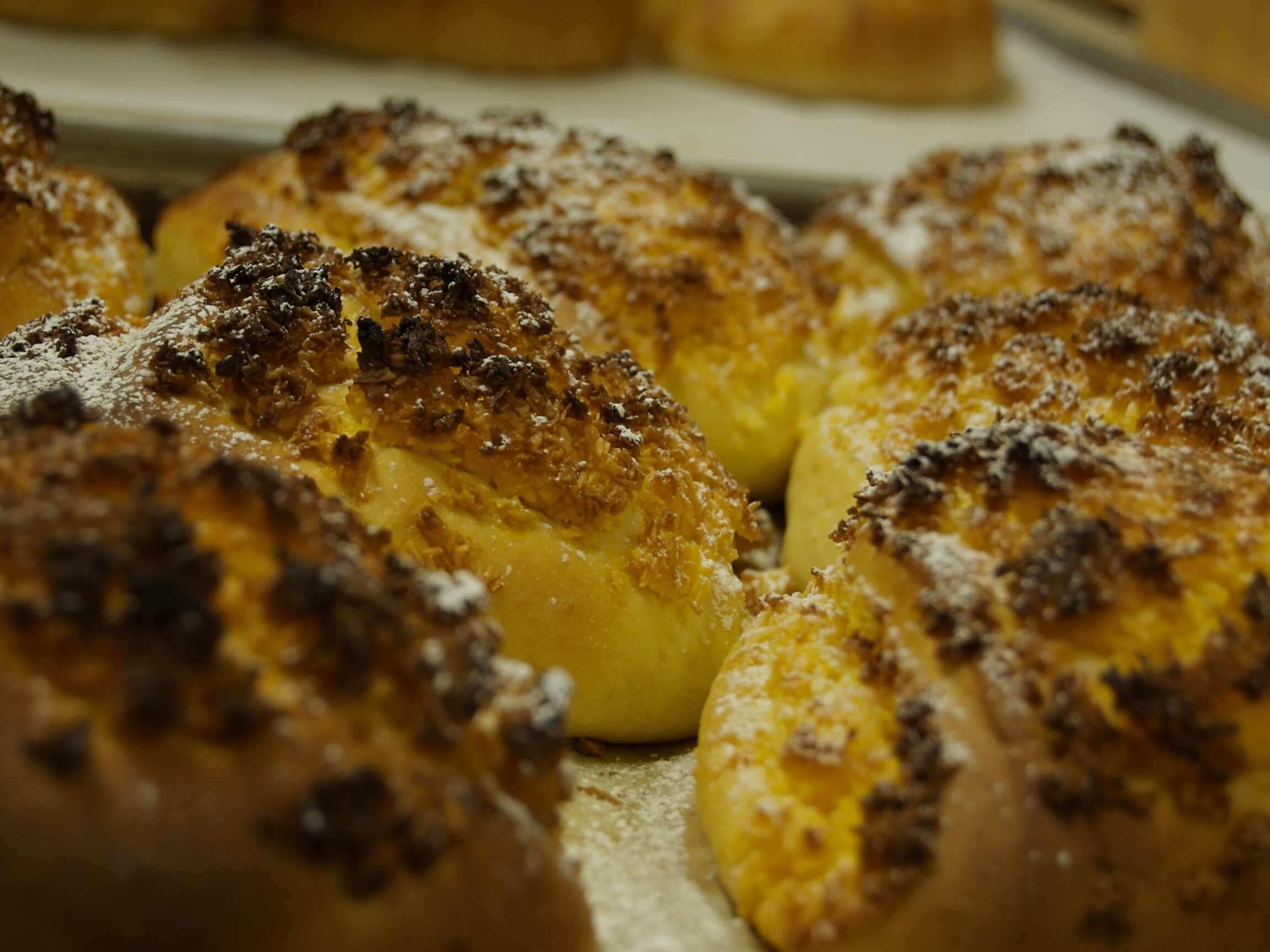 Breads with coconut topping and powdered sugar arranged on a surface.