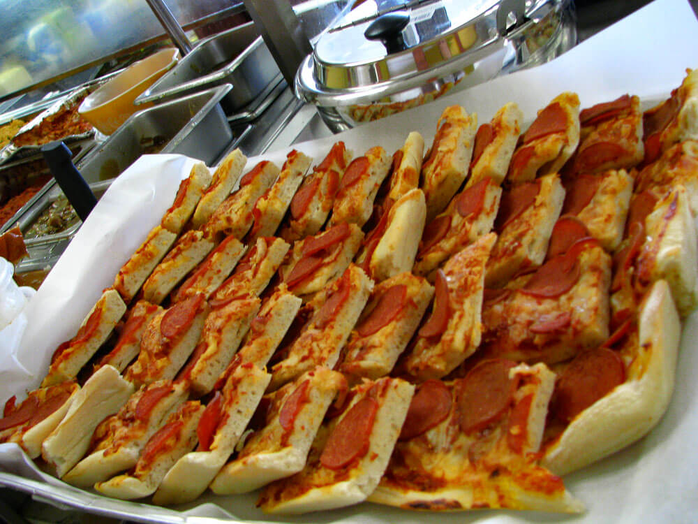 A tray filled with rectangular chorizo breads placed on parchment paper, with several kitchen utensils and containers visible in the background.