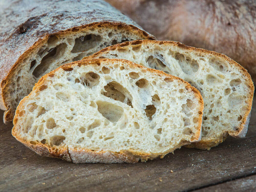 A piece of Mafra bread on a wooden surface, with two slices cut.