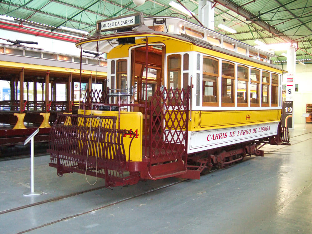 A vintage yellow tram on display at the Carris Museum in Lisbon, showcasing its historic design and intricate metalwork.