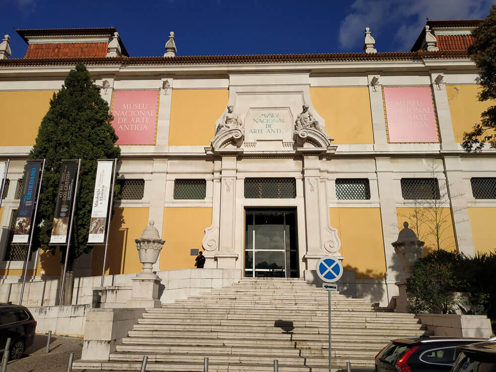 The exterior of the Museu Nacional de Arte Antiga in Lisbon, showcasing its grand entrance, yellow walls, and classical architectural details.