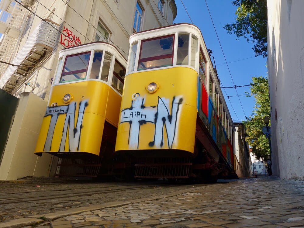 Two yellow funiculars with graffiti, parked on the tracks in Lisbon.