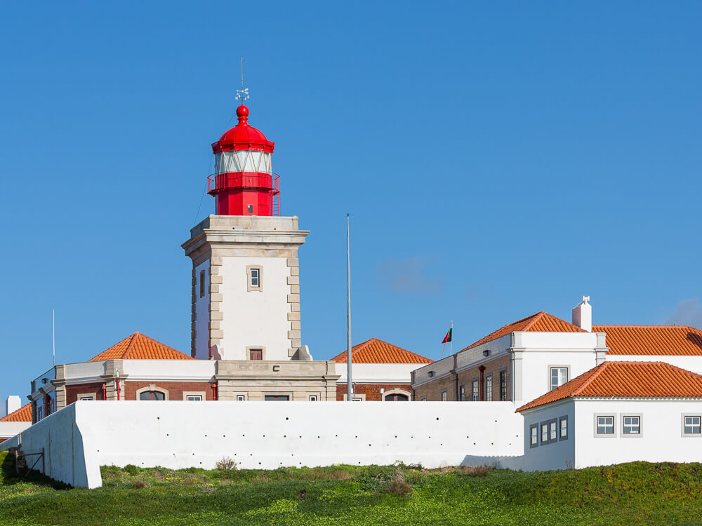 A close-up of a lighthouse with a red dome in Cabo da Roca, set against a clear blue sky.