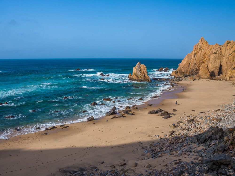 A secluded sandy beach with rocky outcrops and gentle waves, with footprints visible in the sand.