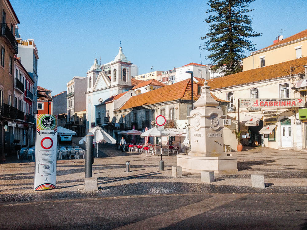 A small square with outdoor tables and chairs, surrounded by traditional buildings, including a church with twin towers.