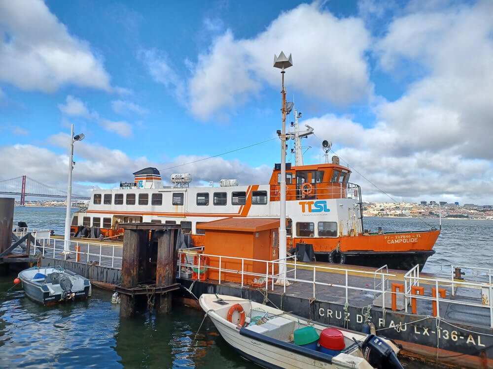 A bright orange and white ferry docked at a port with small boats around, under a cloudy sky.