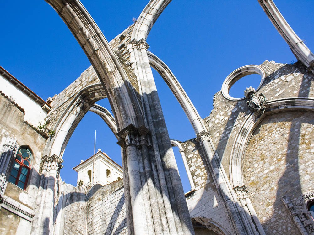 The interior arches of the Carmo Convent ruins in Lisbon, with blue skies visible through the open roof.