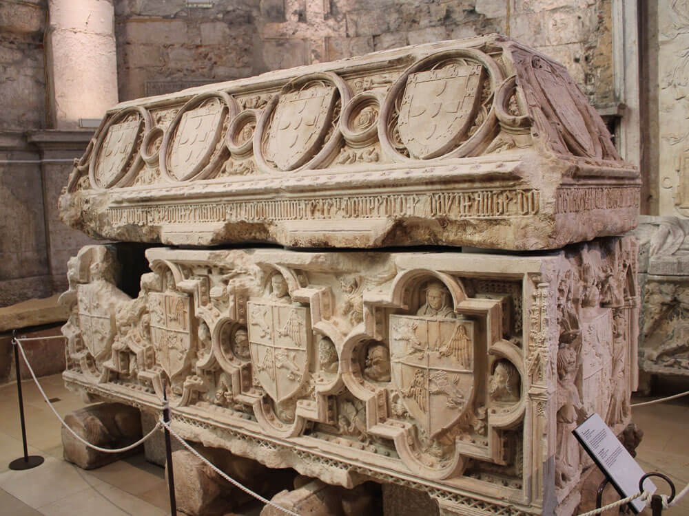 A close-up of a detailed stone sarcophagus inside the Carmo Convent’s museum, showcasing ornate carvings and coats of arms.