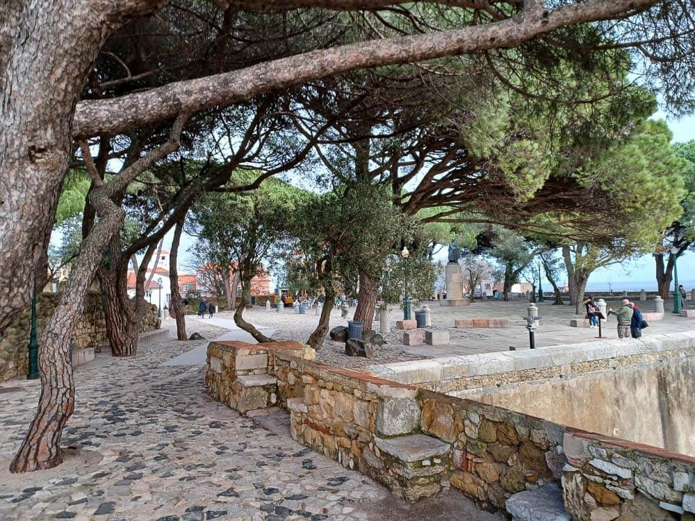 Stone paths and benches under a canopy of trees within the peaceful grounds of Castelo de São Jorge.